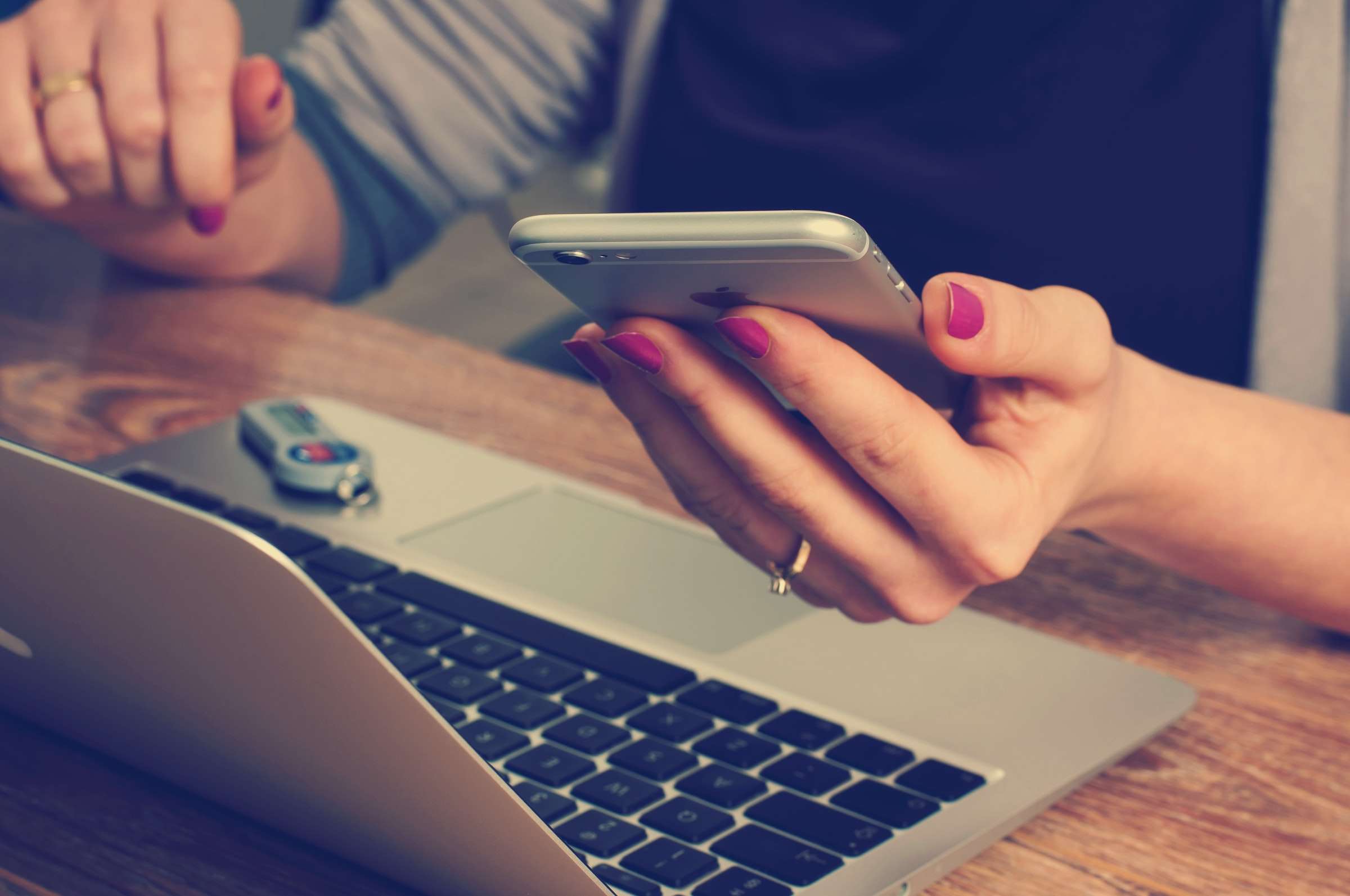 Een vrouw achter haar laptop, ze heeft een telefoon vast